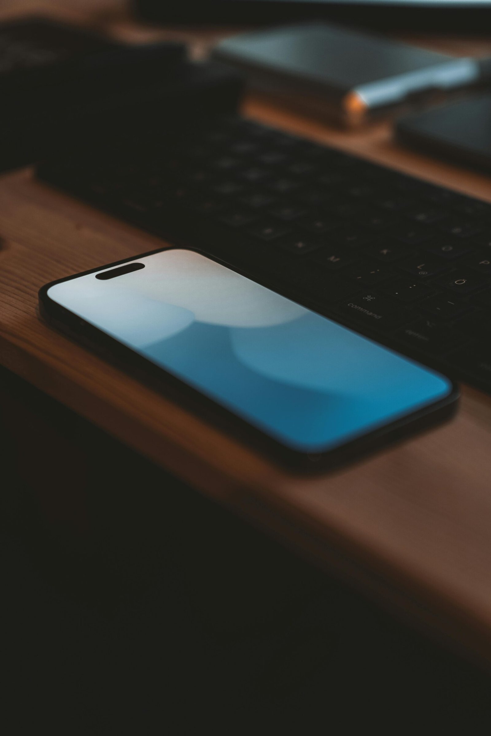A close-up shot of a smartphone on a wooden desk beside a keyboard, highlighting modern technology.